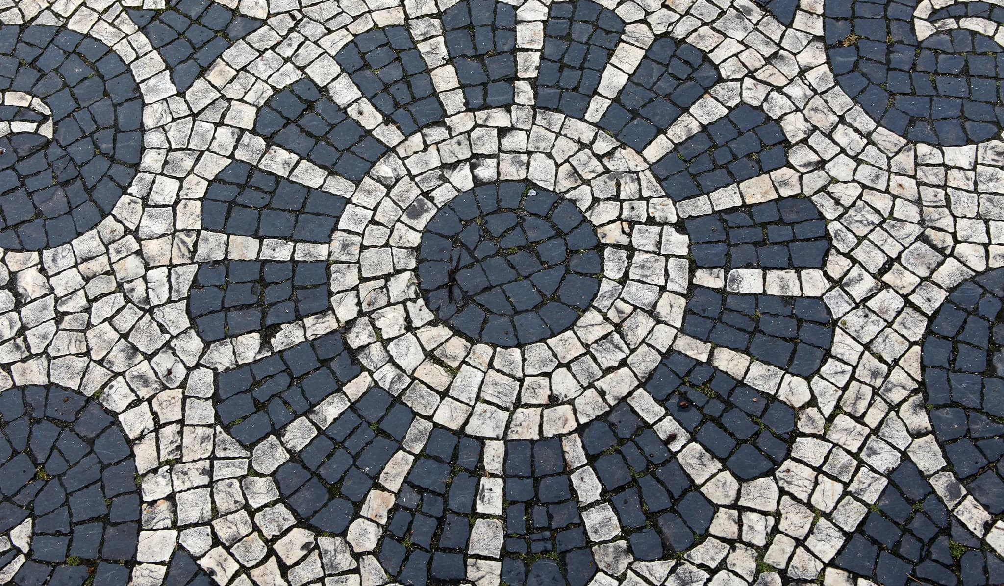 Détail d’un motif circulaire de pavé en pierre blanche et noire, chaque pièce taillée et posée à la main