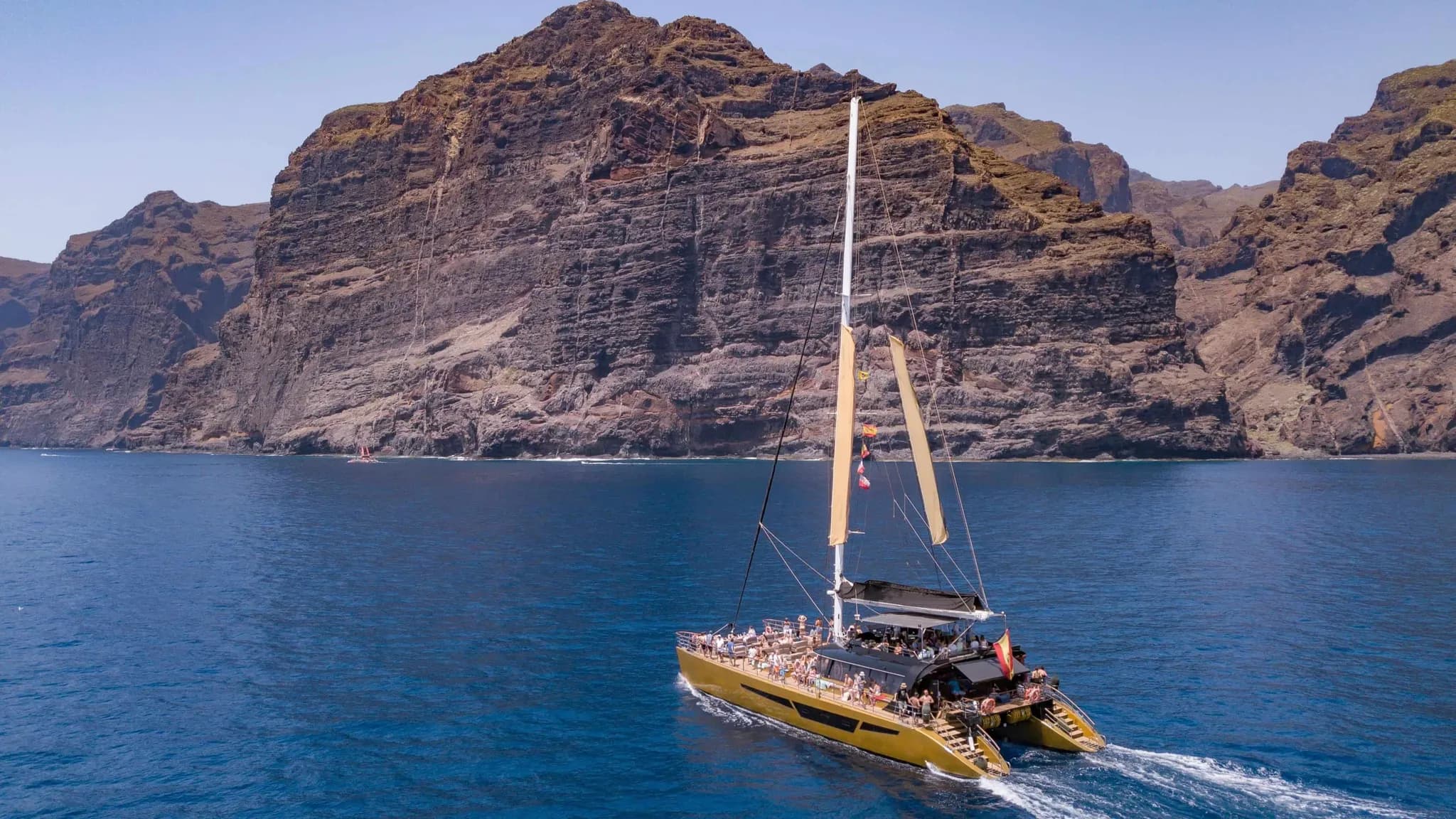Un catamaran rempli d'invités naviguant au pied d'imposantes falaises